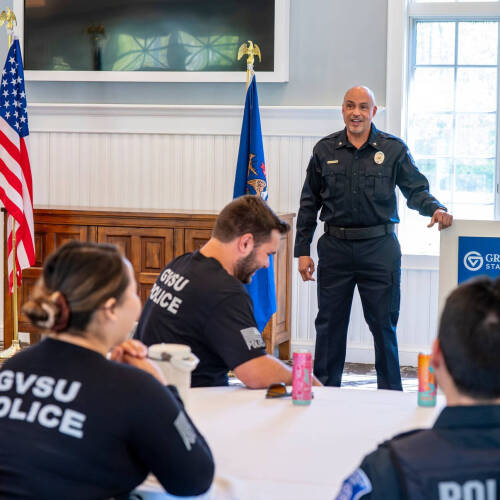 Daniel Lindstrom stands in the Alumni House in front of GVPD officers who are seated at round tables.